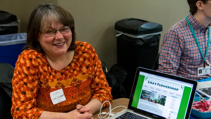 Image of student sitting at a table showing a website on a computer.