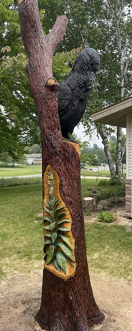 Picture of a carved raven in a tree with a mullein plant